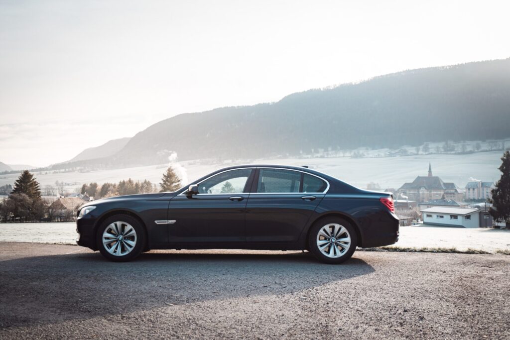 A luxury black car with a professional driver parked in front of a corporate building.